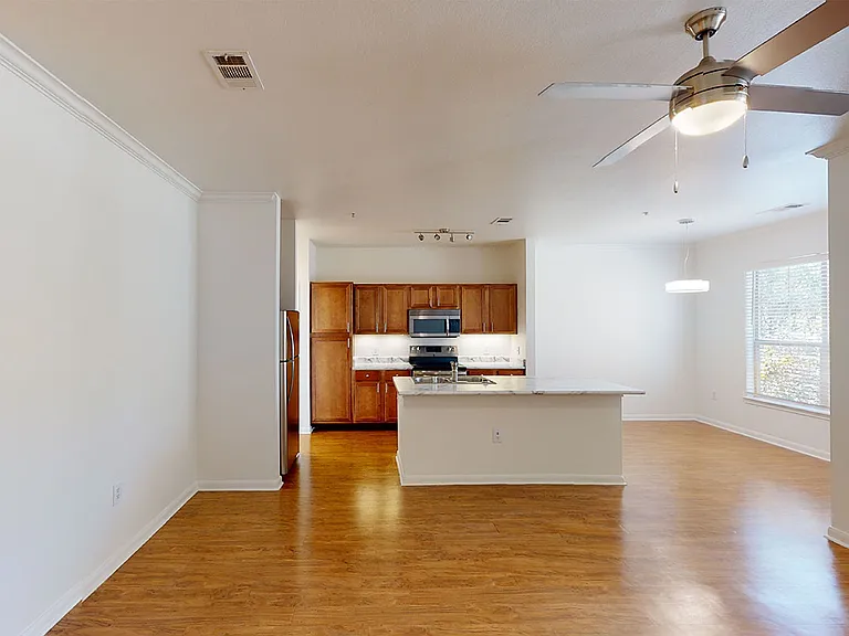 Apartment kitchen with stainless steel appliances, dining and living room with wood-style flooring.