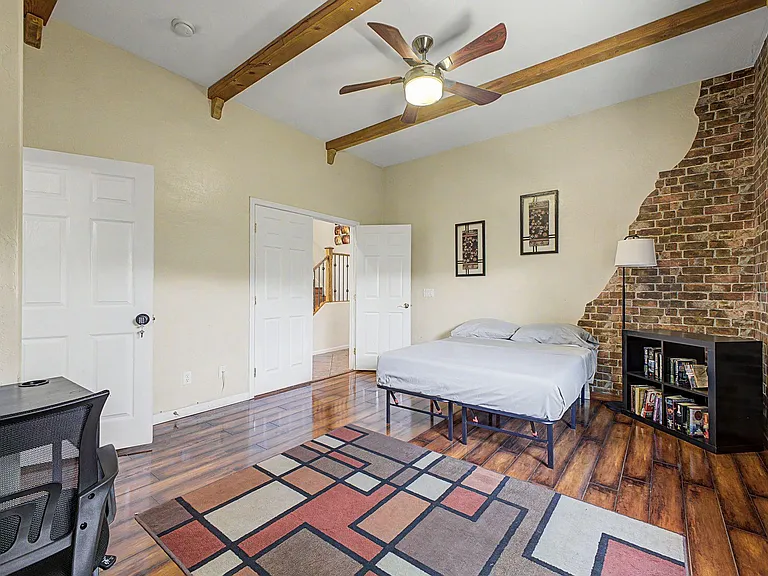 Spacious bedroom with wood-look floors, ceiling fan, and a striking exposed-brick accent wall plus room for a desk.