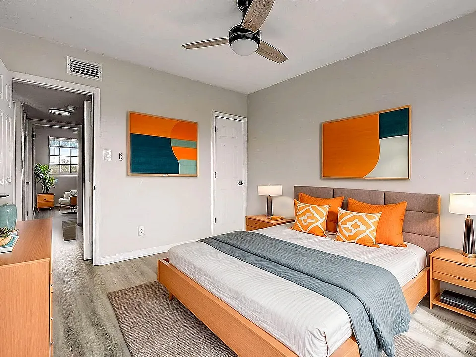 Inviting bedroom with modern decor, featuring a cozy bed with vibrant orange accents, sleek wooden furniture, and abstract wall art.