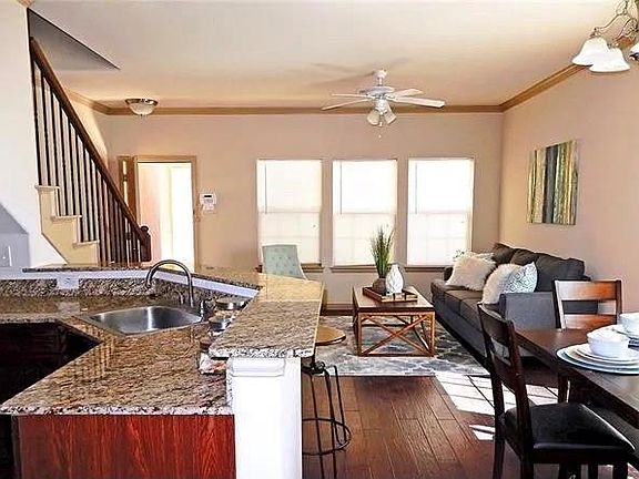 Kitchen with ornamental molding, dark wood-type flooring, light stone countertops, ceiling fan, and open floor plan