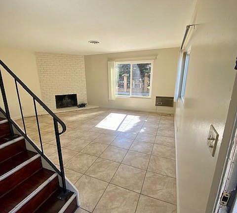 Living room with fireplace and A/C Unit. Tile floors, vertical blinds and new vinyl windows throughout. Tons of natural light, neutral tones.