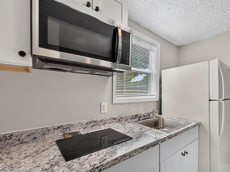 Efficient kitchen workspace with stone-look counters, stainless sink, over-the-range microwave, cooktop, and full-size fridge