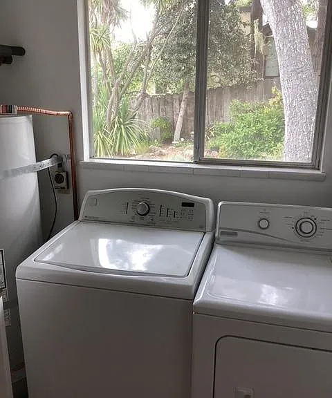 Laundry room with water heater, washer and dryer. Adjacent to kitchen with door for sound reduction. Door to outside yard.