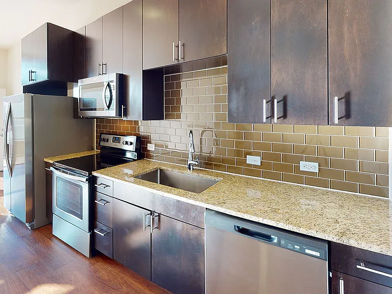 Apartment kitchen with stone countertops, stainless steel appliances, and dark wooden cabinets