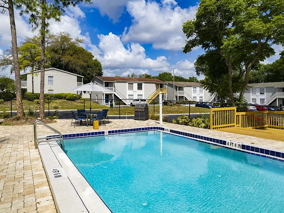 Inviting apartment complex featuring a sparkling swimming pool, surrounded by lush greenery and modern outdoor seating, perfect for relaxation and leisure.
