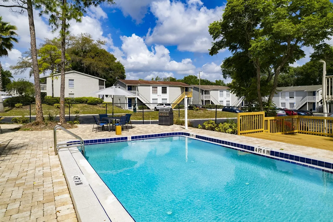 Inviting apartment complex featuring a sparkling swimming pool, surrounded by lush greenery and modern outdoor seating, perfect for relaxation and leisure.