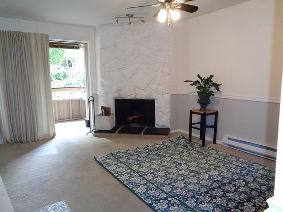 Living room with fireplace, balcony looks out to large area of trees between the buildings