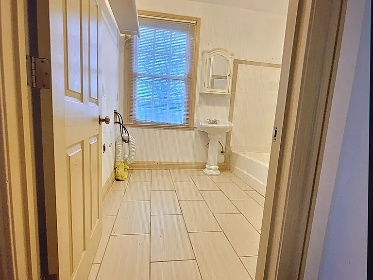 Entrance to bathroom; washing machine & dryer hookups on left with shelving above it