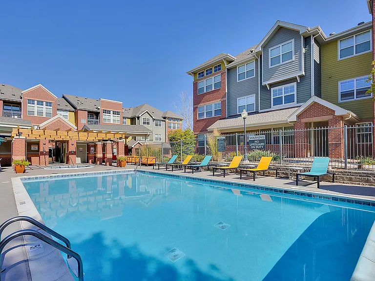 Charming apartment complex with vibrant poolside seating, modern architecture, and a spacious swimming pool under clear blue skies.