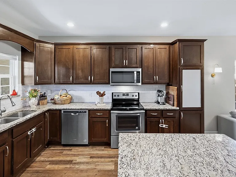 Kitchen featuring wood-finish cabinetry, stainless steel appliances, a double basin sink, light-toned countertops, and wood-finish flooring