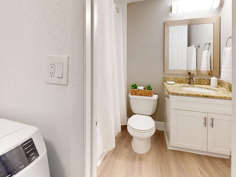 Modern bathroom with elegant granite countertop, sleek fixtures, and adjacent laundry area, creating a stylish and functional space.