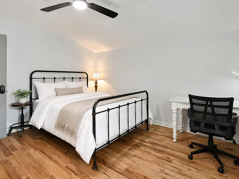 Well-appointed bedroom featuring a metal bed frame, nightstand lighting, and a dedicated desk workspace on hardwood floors.