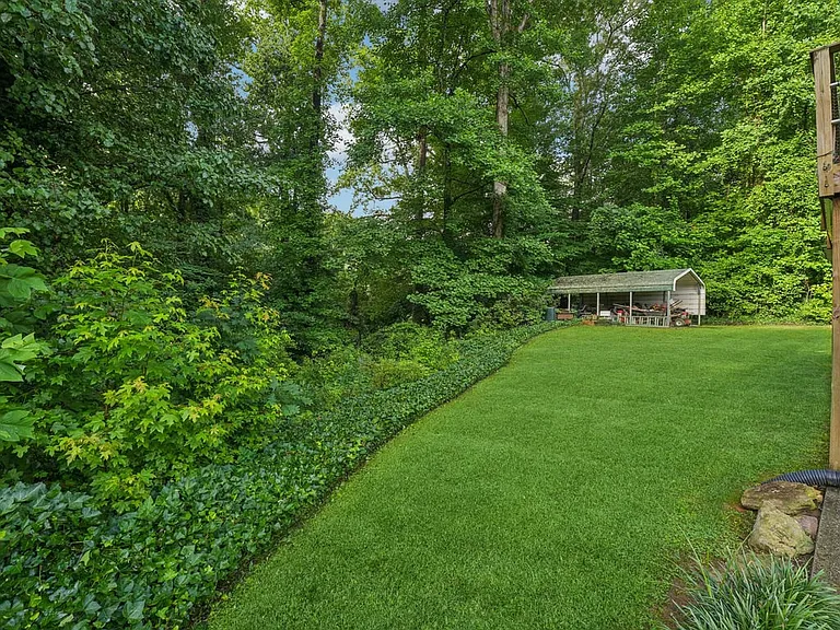 This enchanting rear yard feels like a hidden forest glade, offering open grassy space, mature greenery, and a quiet connection to nature just beyond the home.