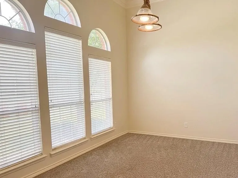 High ceilings featuring a multi-tiered pendant light fixture and a wall of windows, including three arched transoms, with horizontal blinds, and neutral carpet flooring