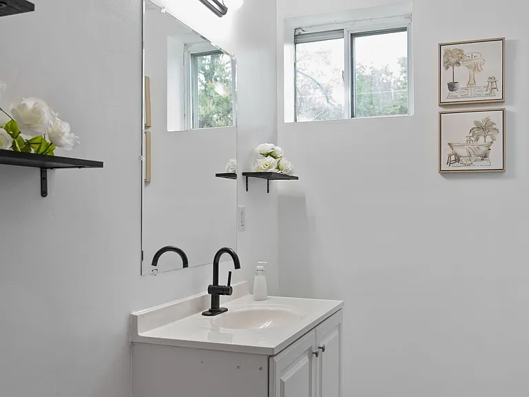 Bathroom vanity area with a single-sink cabinet, large mirror, open shelving, and a window for ventilation.