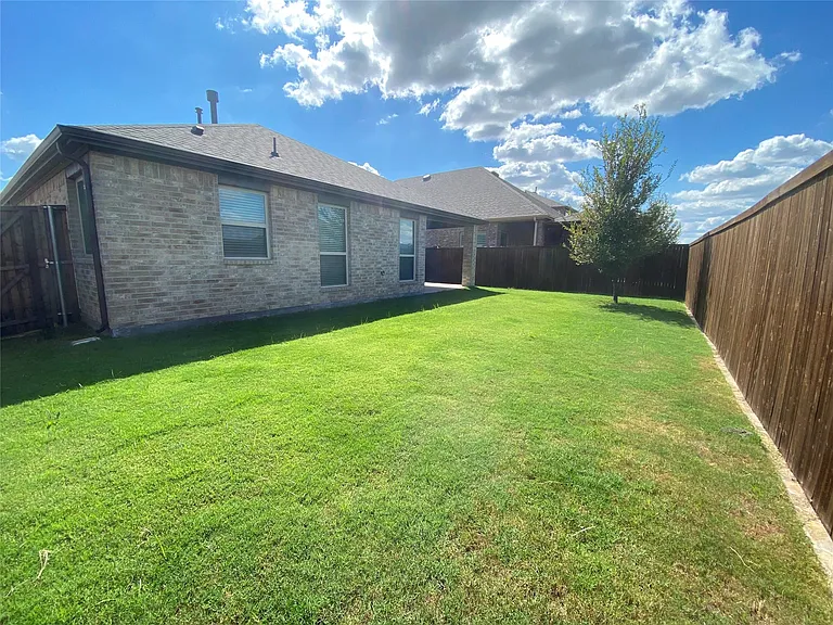 Expansive backyard featuring a manicured lawn, a mature tree, and a covered patio area