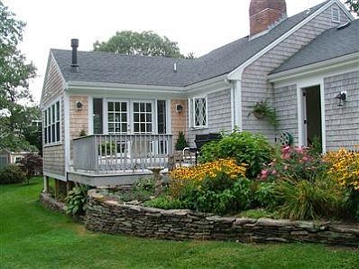 Newly constructed stone wall surrounds a lush, colorful garden bed running along the shell covered pathway.