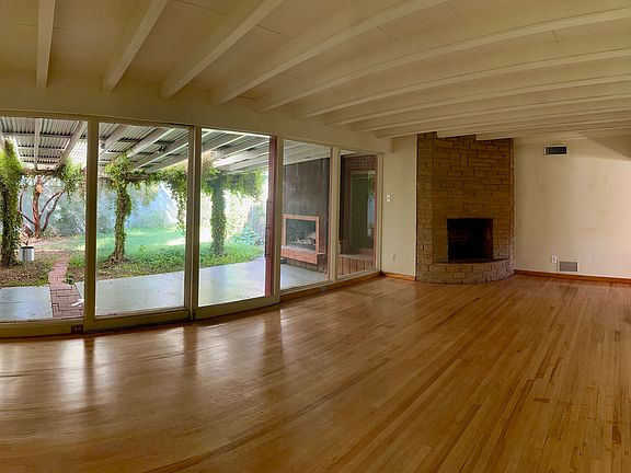 Large living room with floor-to-ceiling windows, sliding glass door to patio, original hardwood floors and fireplace