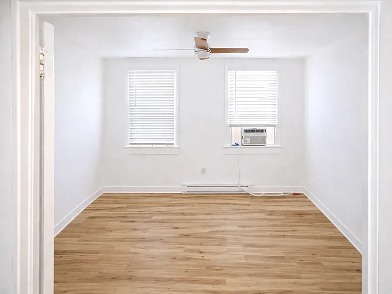 Second bedroom with wood-style flooring, modern ceiling fan, personal A/C unit, baseboard heating, and a walk-in closet