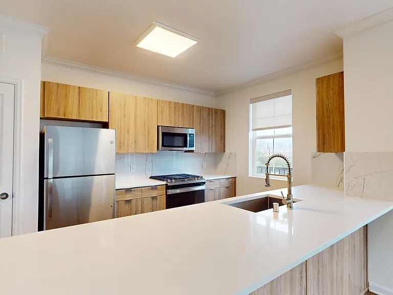 Apartment kitchen with Stainless Steel Appliances, light counters, and wood style floor.