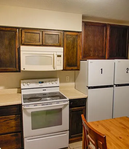 Efficient shared kitchen with ample wood cabinetry, electric range with microwave, and refrigerator access.