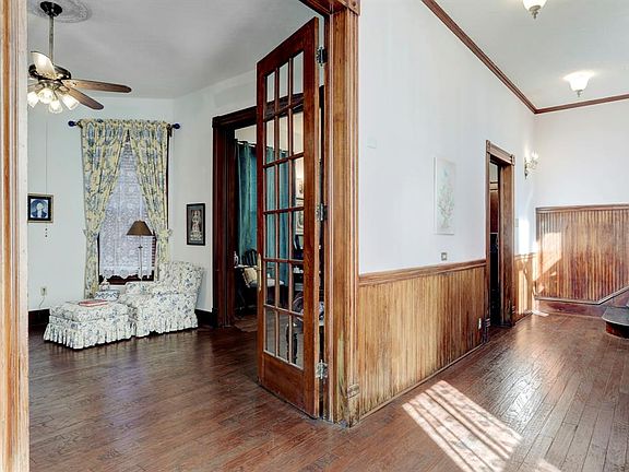 Front foyer with formal living room to the left through French doors. Entry from the foyer to the dining room further down. Original wainscoting in the foyer and up the staircase at the end of the foyer. There is a powder room under the stairs. Origi