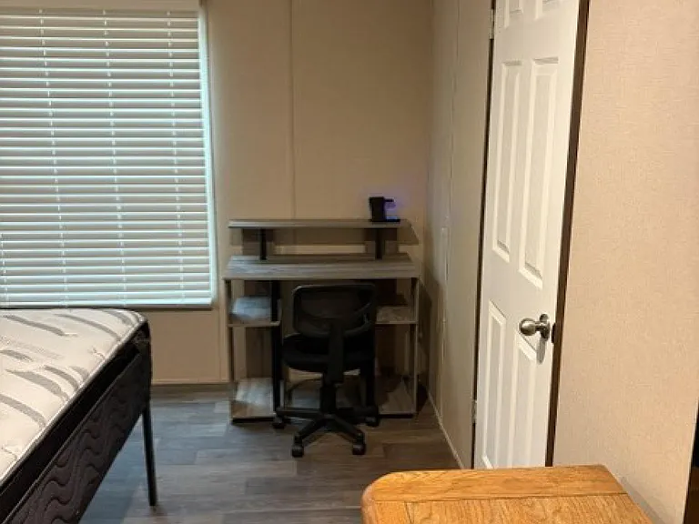 Private bedroom with a window for natural light, durable flooring, and space for a bed plus a compact desk/work area.