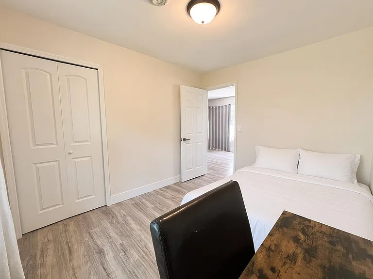 Furnished bedroom with a full bed, work desk, and double-door closet, plus easy access to the hallway and natural light.