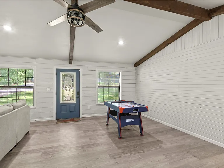 Spacious room featuring wood-finish flooring, white shiplap walls, and exposed ceiling beams