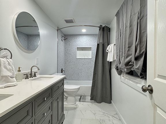 Full bath with a long double-sink vanity, generous counter space, and a tub/shower combo with tiled surround.