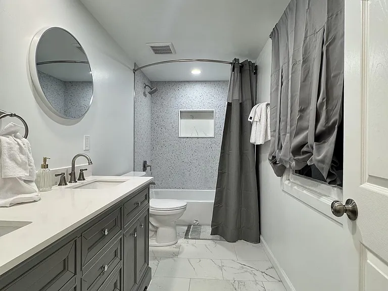 Full bath with a long double-sink vanity, generous counter space, and a tub/shower combo with tiled surround.