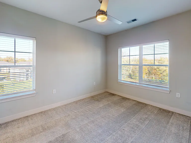 The Dogwood's primary bedroom includes several windows, a ceiling fan, and soft carpet. The Dogwood's primary bedroom includes several windows, a ceiling fan, and soft carpet.