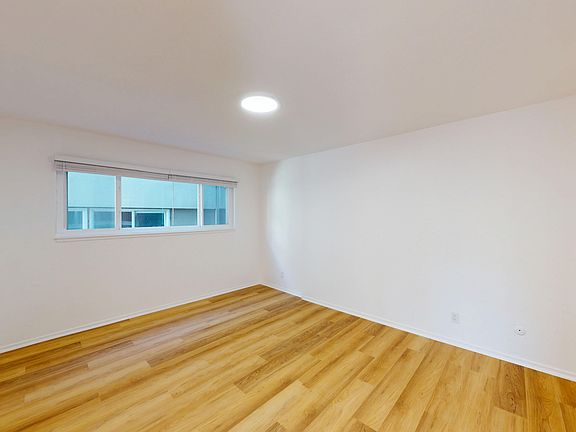 Room with wooden flooring, window with blinds, and ceiling light fixture