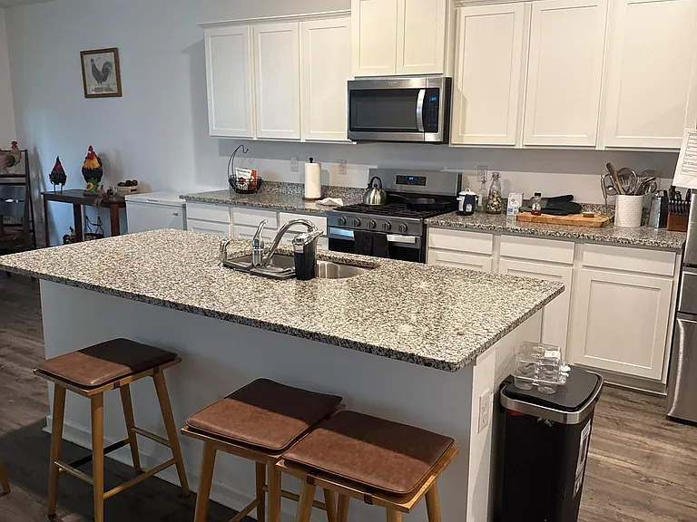 Open kitchen with a large breakfast bar, granite-look counters, ample white cabinetry, and stainless steel appliances.