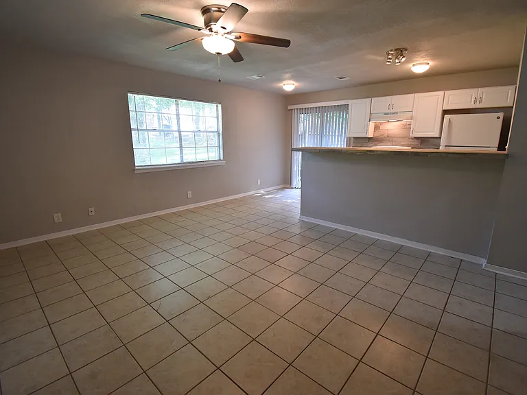 Open Floor plan! Living room with large windows and a ceiling fan. Kitchen and Dining room in the background.