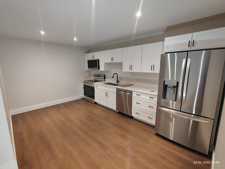 Full kitchen features brand-new stainless appliances_including a French-door refrigerator, range/oven, microwave, and dishwasher_plus quartz countertops, soft-close cabinetry, and room for a dining table.