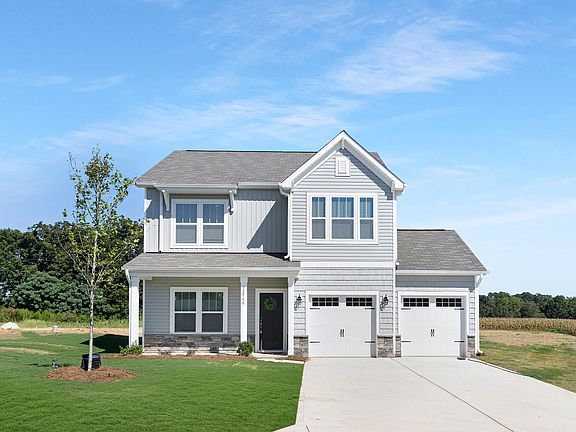 A white house with a gray roof is sitting on top of a lush green field.