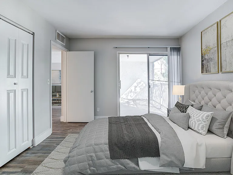 Bright and airy bedroom with plush gray bedding, elegant decor, and access to a private balcony for serene outdoor views.