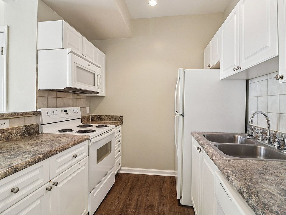 Modern apartment kitchen featuring sleek white cabinetry, stylish countertops, and stainless steel appliances, including a microwave and electric stove.