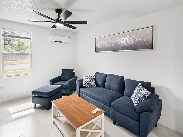 Living room with a comfortable seating set, ceiling fan, and a large window that brings in natural light.
