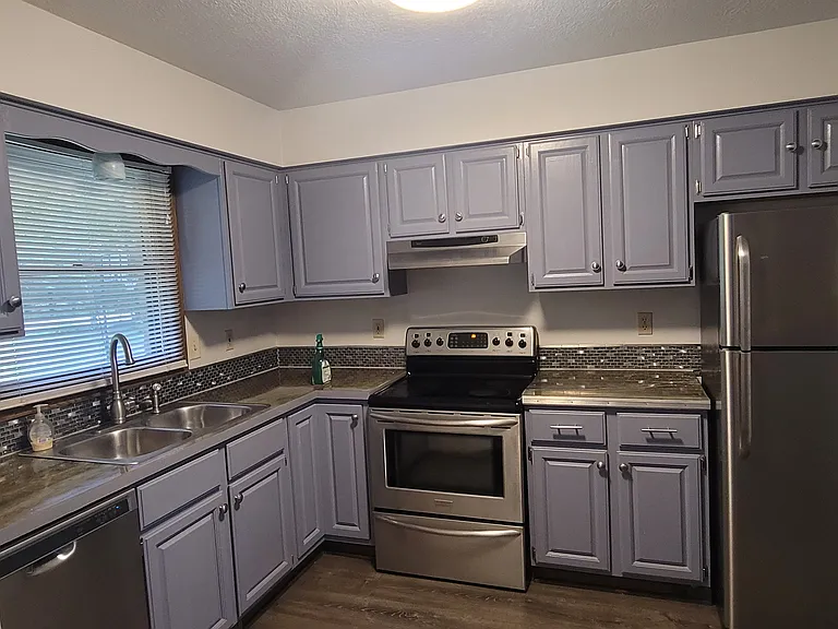 Looking in from the main entrance on the left hand side is the kitchen with bluish-gray cabinets and stainless steel appliances.