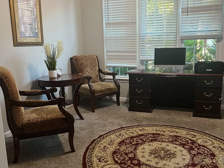Furnished flex room with large windows and blinds, plus a dresser and seating areaideal for a home office or lounge.