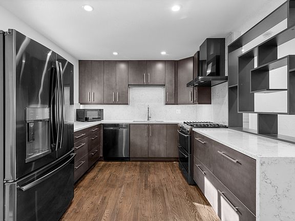 The kitchen features quartz countertops with a striking waterfall edge, stainless steel appliances, and a gas range.