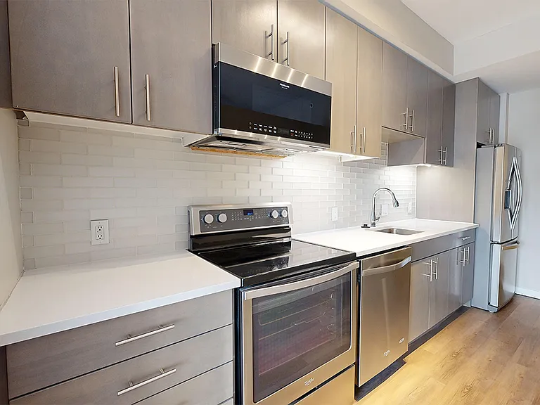 Apartment kitchen with stainless steel appliances, quartz countertops and wood-style flooring.