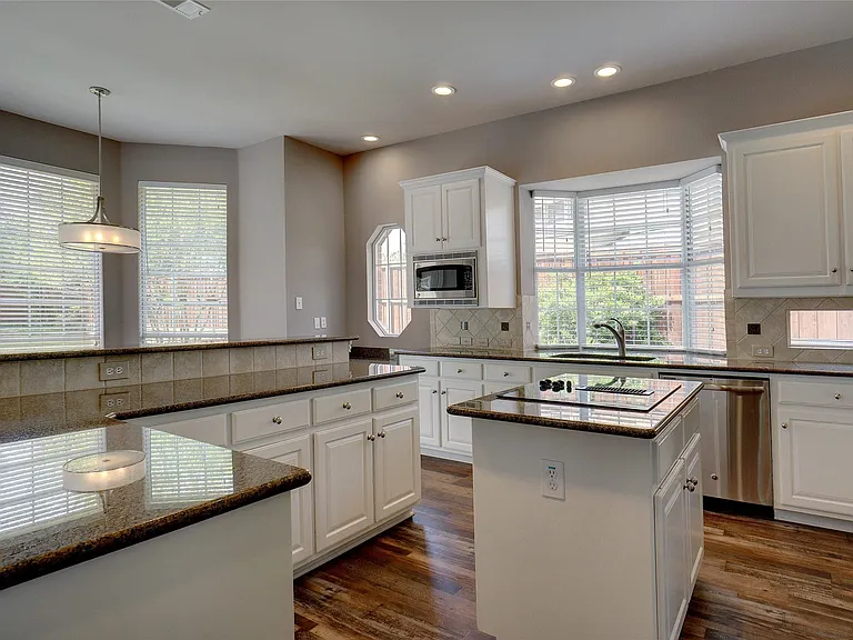 Kitchen featuring white cabinetry, dark stone countertops, wood-finish flooring, a central island with cooktop, and stainless steel appliances