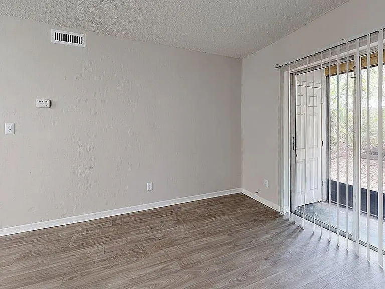 Bright and inviting living space with elegant wood flooring, large sliding glass doors leading to a serene outdoor view, and modern bathroom access.