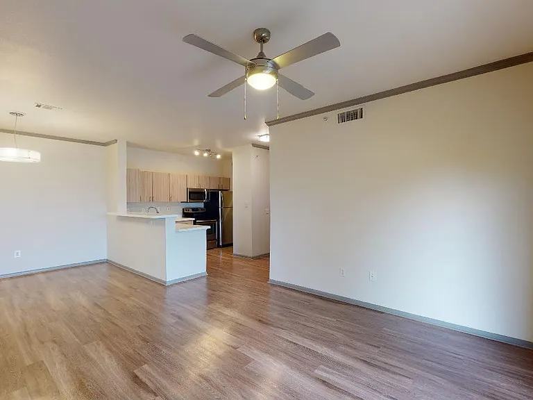 Apartment kitchen with stainless steel appliances, dining and living room with wood-style flooring.