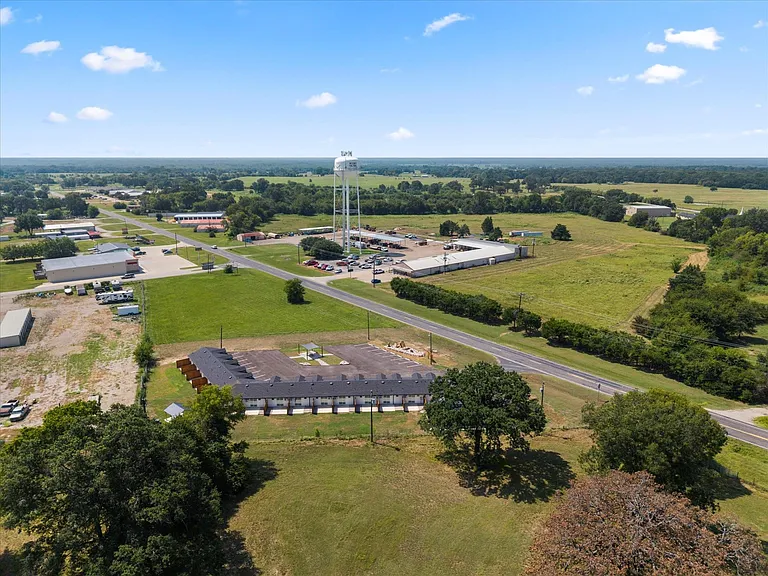 An aerial perspective showcasing a multi-unit property with dark shingle roofing, surrounded by expansive green spaces