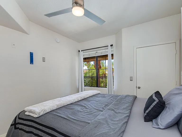 Well-sized bedroom with a ceiling fan, comfortable bed space, and a large window with curtains and pleasant outdoor views.