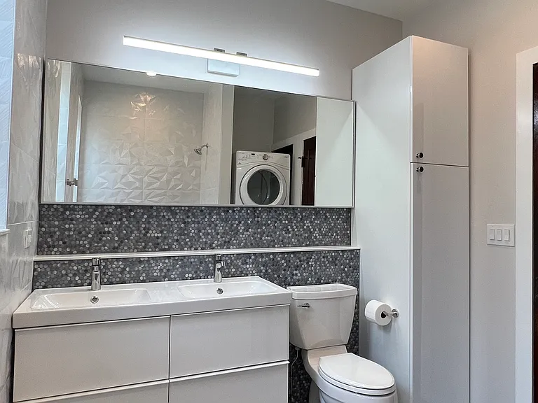 Modernized bathroom with double vanity, linen closet, tub and shower, and washer dryer.